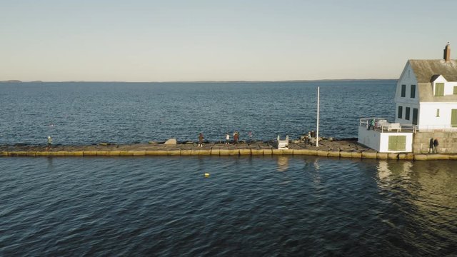 Tourists walking along a breakwater towards a lighthouse at sunset AERIAL SLIDE