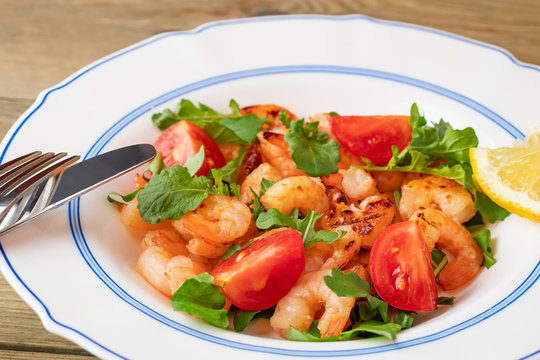 Fresh homemade salad of shrimp, arugula and tomato in a white plate on a wooden table, close up