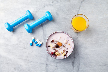 Bowl of granola with yogurt, nuts, raisins, cranberries and chia seeds. Blue dumbbells and sports supplements in background. Concept for a tasty and healthy meal. Stone background. Copy space