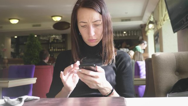 Young wonam use mobile phone while sitting in comfortable coffee shop during work break, charming happy female reading fashion news on cell telephone during breakfast in restaurant.