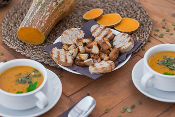 Rustic table with a raw pumpink in the middle of  it. Healthy eating in autumn and winter time. Wooden table with two bowls of pumpkin cream soup.