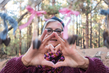 Love of nature Caucasian senior woman forming a heart with their hands in the forest. Human hands in the light of dusk