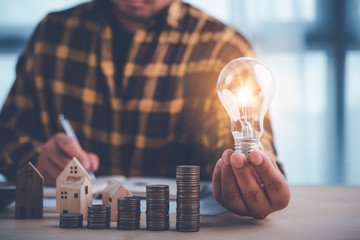 businessman hand holding lightbulb with coins stacking on desk.saving energy and money concept.