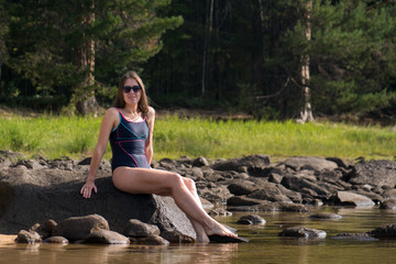 A girl in a swimsuit sits on the shore of Lake Baikal