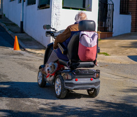 Elderly disabled person or senior with a dog on electric wheelchair or a mobility scooter driving on road. An elderly person is always together with his pet. Modern technology for people disabilities.