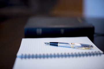 Closeup shot of a fountain pen on a notebook with a blurred bible in the background
