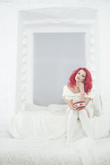 Fototapeta na wymiar cute red hair woman in cozy knitted white sweater dress relax on the fur bed in her white room