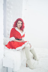 Fototapeta na wymiar pretty redhaired young stylish woman in velvet santa dress with fur posing on white room background near the cozy window