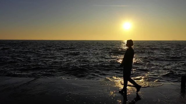 Slow motion female walking by the ocean with waves on sunset