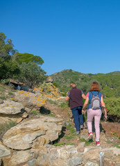 Elderly, senior couple travelling together in the mountains of Catalonia on blue sky background. Couple hikers climbs a mountain path. Healthy, active lifestyle at any age. Walking trails, hiking.