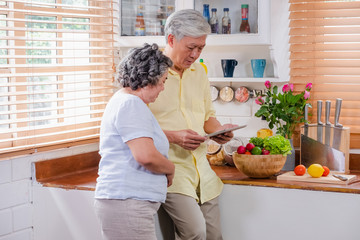 Asian senior couple using tablet computer to searching menu recipe and type of vegetable in kitchen at home.senior with technology lfiestyle.aging at home