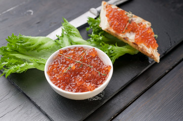 Close-up sandwich with butter, red salmon caviar and lettuce on a black background. Gourmet breakfast