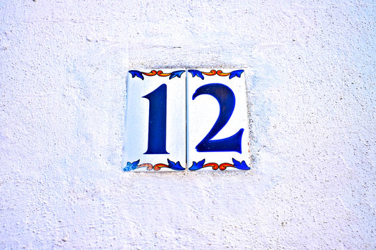 Simple number 12, twelve, plain floral tiles on a white wall with slight blue cast.