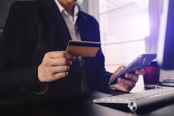 businessman hand using smart phone, tablet payments and holding credit card online shopping, omni channel, digital tablet docking keyboard computer at office in sun light
