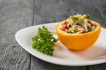 Half an orange filled with salad on a white plate with a sprig of parsley.