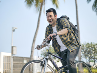 Motion blur happy Asian man with backpack riding bicycle with green tree - Powered by Adobe