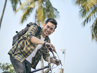 Fototapeta na wymiar Happy Asian man with backpack riding bicycle with green tree