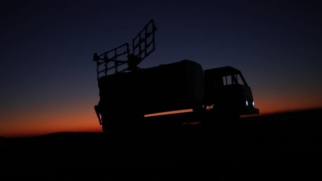 Creative artwork decoration. Silhouette of mobile air defence truck with radar antenna during sunset. Satellite dishes or radio antennas against evening sky. Selective focus