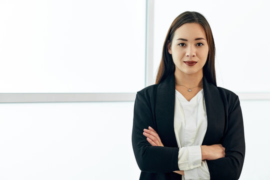 Smiling asian business woman in modern office on white background. crossed arms.