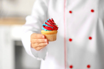 Fototapeta na wymiar Female confectioner with tasty cupcake in kitchen, closeup