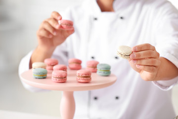 Male confectioner with tasty macarons in kitchen, closeup