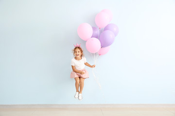 Jumping little girl with balloons on color background © Pixel-Shot