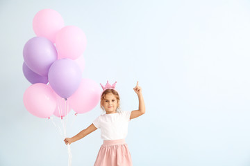 Little girl with balloons and raised index finger on color background