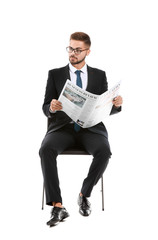 Handsome businessman with newspaper sitting on chair against white background