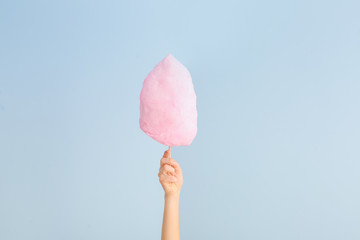 Female hand with tasty cotton candy on light background