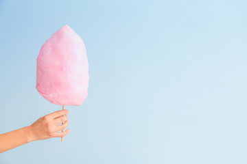 Female hand with tasty cotton candy on light background