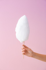 Female hand with tasty cotton candy on color background