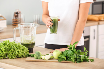 Woman with glass of healthy smoothie in kitchen