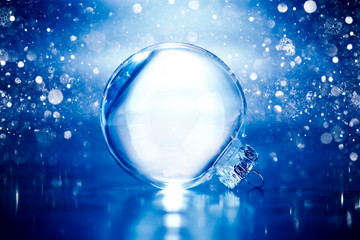 Clear glass Christmas ornament on blue glittering lights background with blank empty space