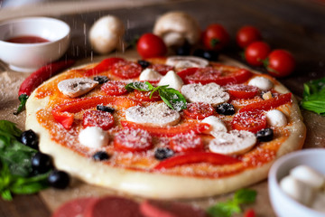 close up of uncooked pizza with mushrooms, peppers, olives and mozzarella sprinkled with Parmesan