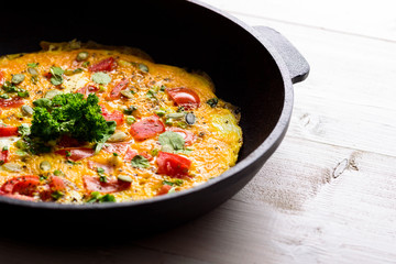 Macro close up omelet with tomatoes and greens in a cast iron pan on a white background