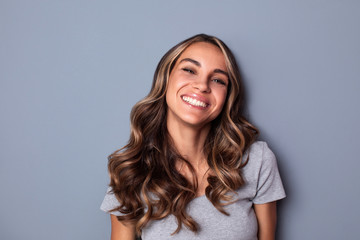 Fototapeta premium Beautiful smiling woman with clean skin, natural make-up, and white teeth on grey background.