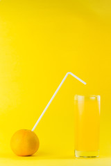 orange with straw next to a glass of orange juice isolated  on a orange colored background with copy space