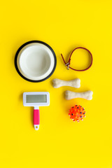 Pet's accessories like bones, collar and bowl on yellow background top view flat lay