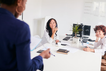 View from back of speaker coach, asian and caucasian positive smiling women sitting on table listen to new business plan by coach