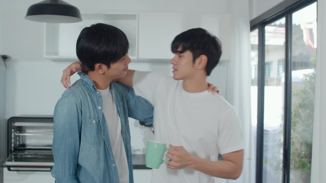Asian gay couple drinking coffee, having a great time at home. Young handsome LGBTQ+ men talking happy relax rest together spend romantic time in modern kitchen at house in the morning concept.