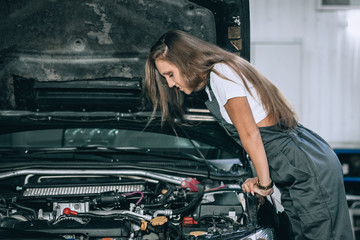 Naklejka na ściany i meble Pretty brunette from car service in a black jumpsuit and white t-shirt standing near the broken car. The girl opened the hood and looked at the engine. Refit woman car