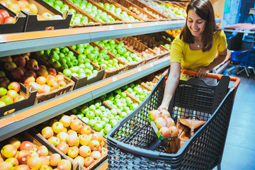 young pretty adult woman do shopping in grocery store buying apple