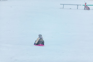 Fototapeta na wymiar little kid at sledge sliding down by winter hill