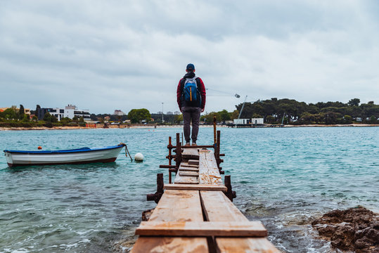 man standing at edge of the small fishing pier looking at stormy sea