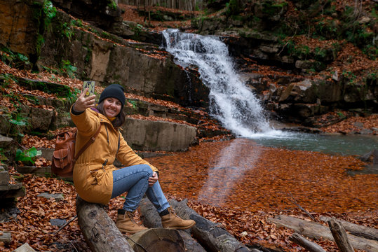 woman sitting on the log looking at waterfall autumn season