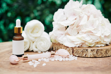 Light pink hydrangea flower, quartz massage roll and rejuvenating essence on wood stump