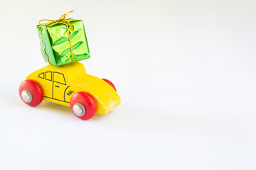 Green gift box with golden ribbon on yellow wooden car on white background with copy space. Christmas and new year concept.