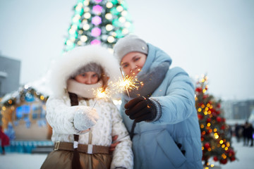 Woman and teenager girl with Christmas sparklers in winter clothes on the street.