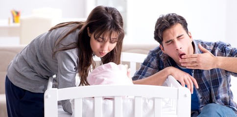 The young parents with their newborn baby near bed cot