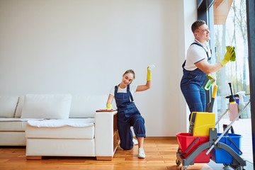 Man cleaning panoramic window and girl polishing sofa. Teamwork of cleaning company.